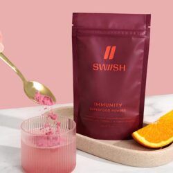 Immunity Superfood Powder pouch with hand dropping a spoonful of powder into a glass of water
