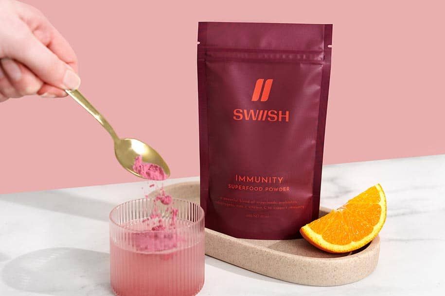Immunity Superfood Powder pouch with hand dropping a spoonful of powder into a glass of water