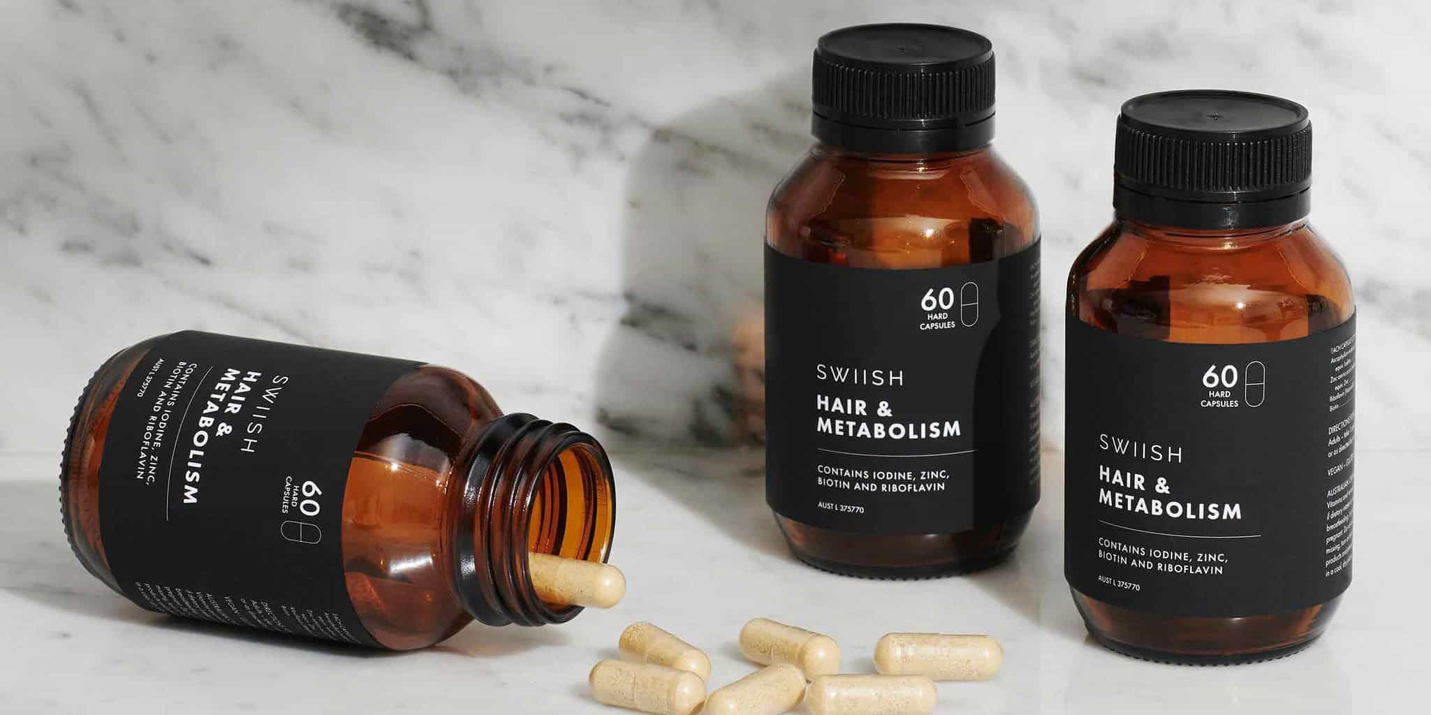 Three bottles of SWIISH Hair & Metabolism supplement with one bottle lying on its side with capsules spilling out