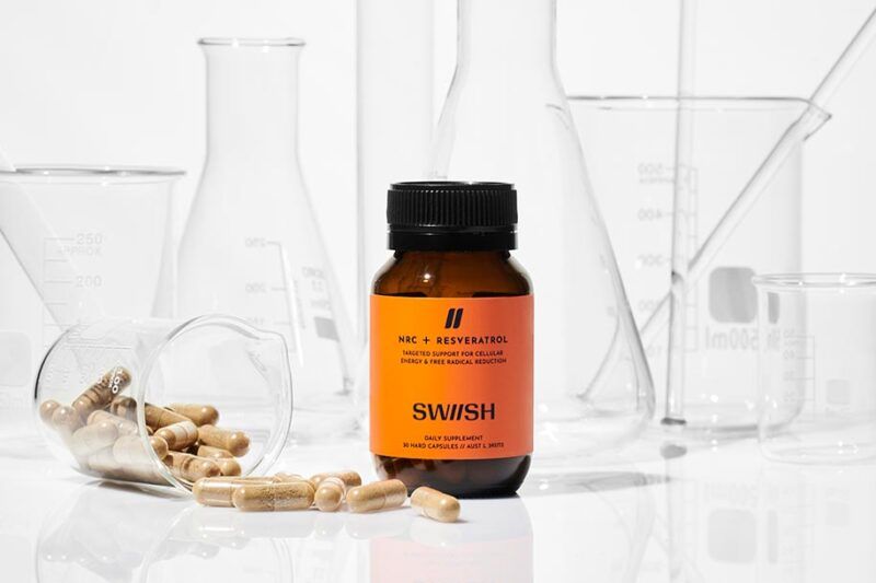 SWIISH NRC + Resveratrol supplement bottle in front of science lab equipment and test tubes and beakers with capsules spilling out of bottle
