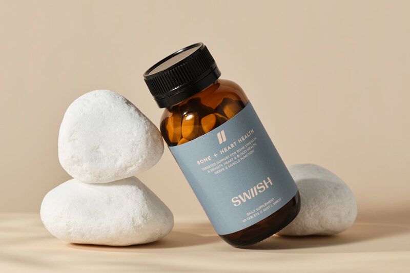 Bottle of SWIISH Bone + Heart Health supplement styled with 3 white stones on a neutral background